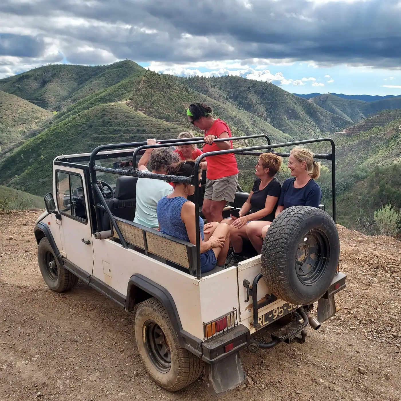 Guests in the back of the open jeep, parked on a ridge with green hills rolling away behind