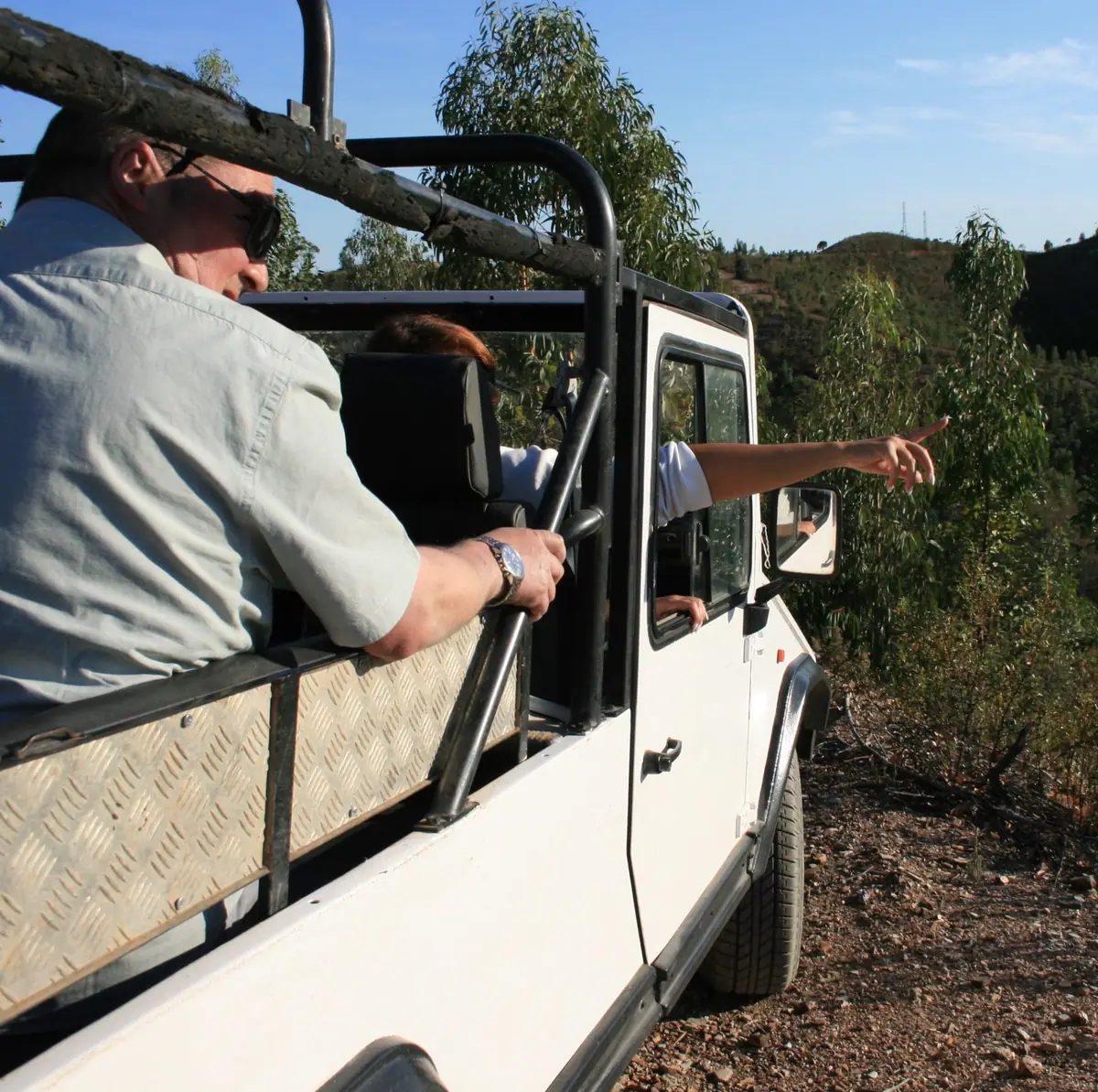 Thyl at the wheel of the open jeep, a guest pointing out over the hills